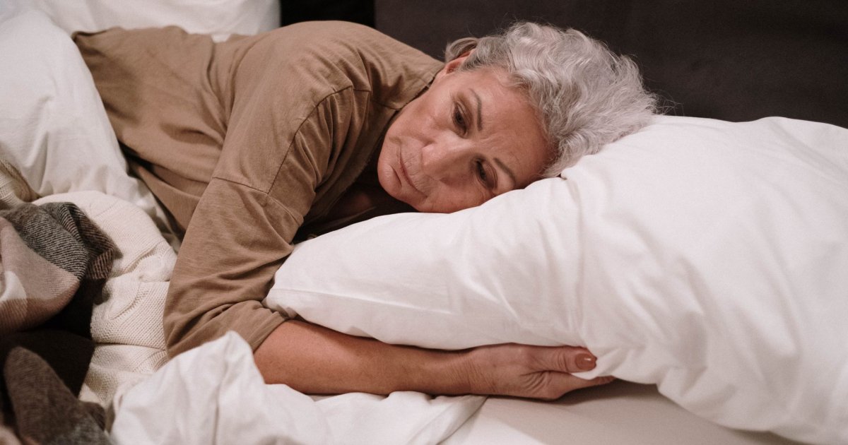Donna di mezza età a letto che non riesce a dormire, simbolo di menopausa e insonnia