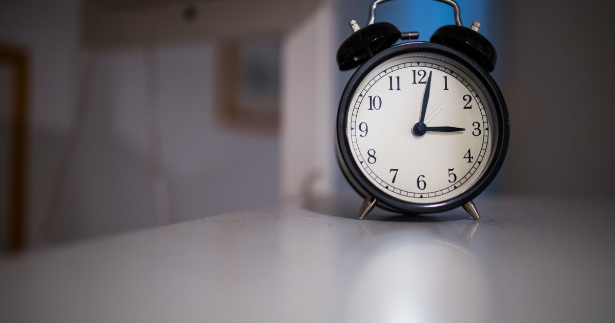 Donna sveglia a letto di notte che guarda l'orologio con espressione preoccupata, concetto di insonnia e risvegli notturni.